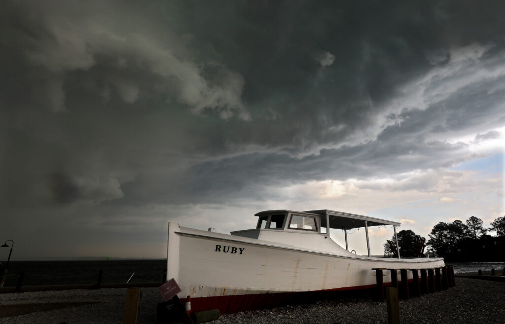 Dark storm clouds loom over the Rappahannock River as a white boat named Ruby rests on the gravel shoreline