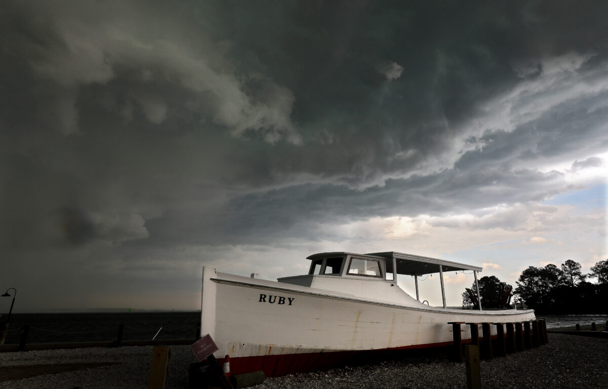 Dark storm clouds loom over the Rappahannock River as a white boat named Ruby rests on the gravel shoreline